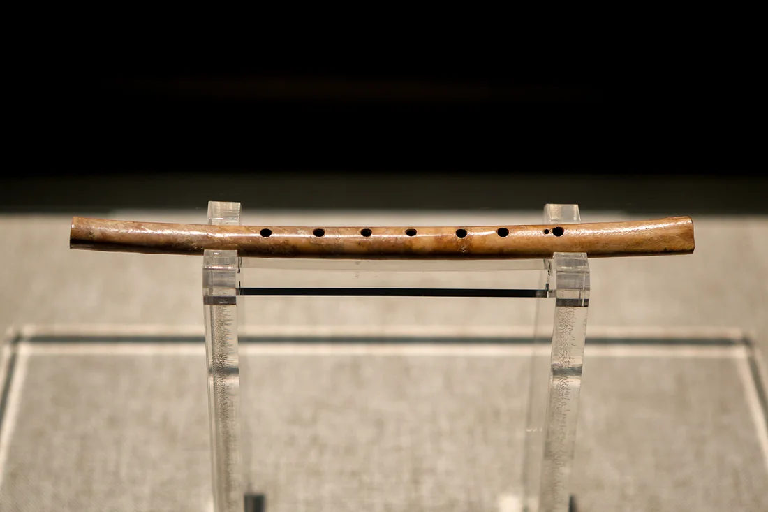 Flûte en os de Jiahu exposée en vitrine, os long et fin percé d'une série de trous régulièrement espacés.