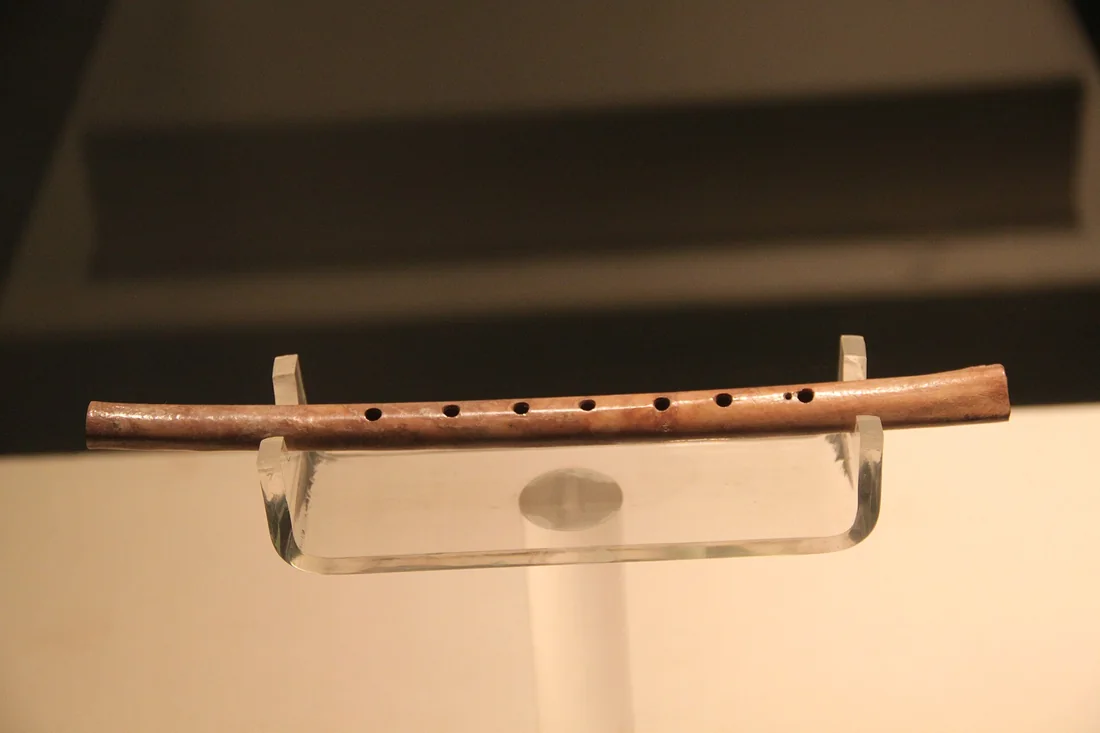 Flûte en os de la culture de Peiligang exhumée à Wuyang, présentée en vitrine avec sa rangée de trous de jeu.